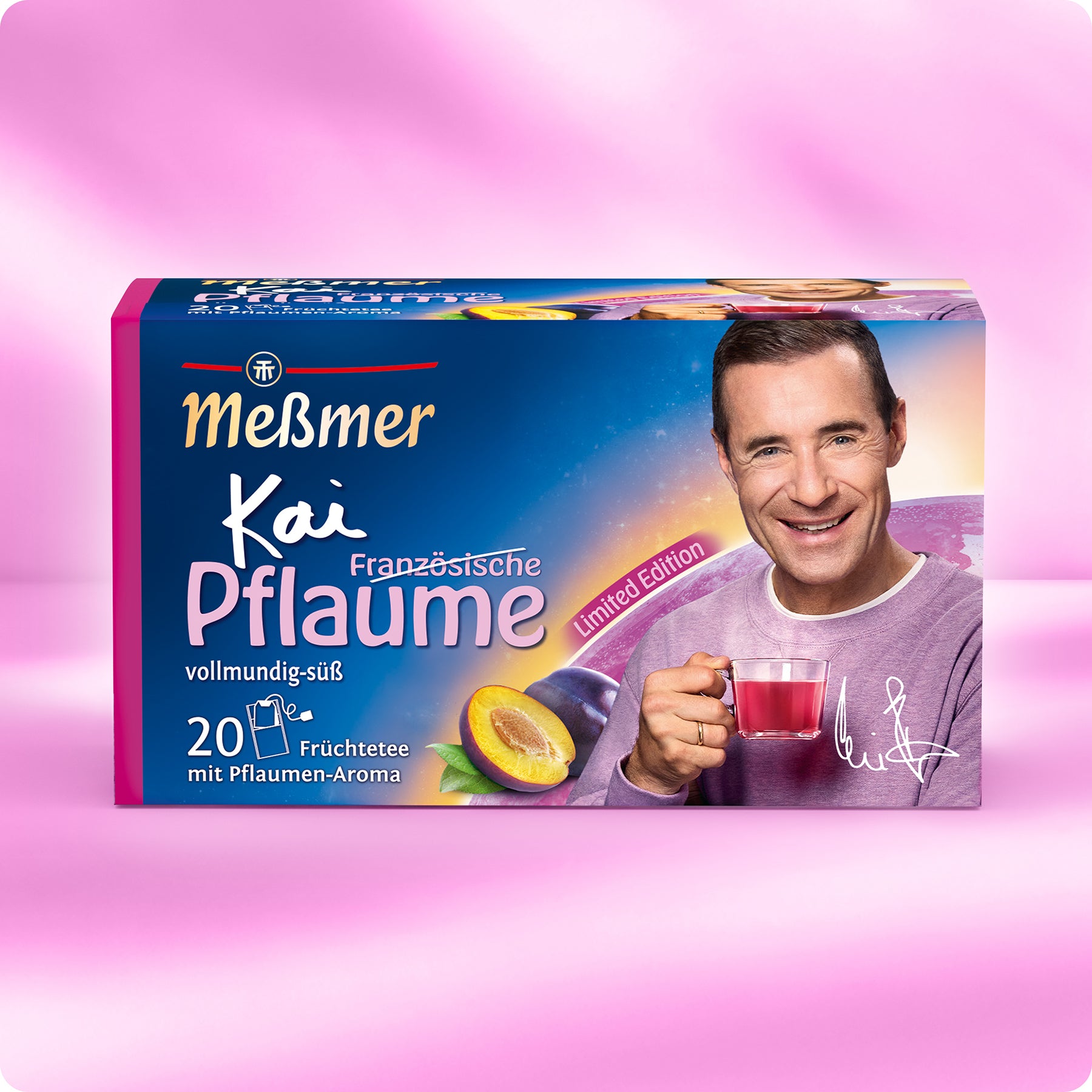 Eine Schachtel Meßmer-Tee mit Kai Pflaume auf der Vorderseite, der eine rote Tasse hält. Die Verpackung ist rosa und lila mit Abbildungen von Pflaumen und Tee, mit der Aufschrift "Französische Pflaume" und "Limited Edition".