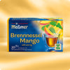 Verpackung von Brennnessel-Mango Tee mit Darstellung einer Tasse goldbraunen Aufguss, frischer Mangoscheiben und Brennnesselblättern, Hinweis auf süß-würzigen Geschmack und Care-for-Tea-Siegel.