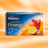 Eine Meßmer DE Spanische Orange Schachtel zeigt ein Glas Orangentee mit Orangenscheiben auf einem lebendigen Hintergrund, der 20 Früchteteebeutel und den kräftigen Geschmack der Spanischen Orange hervorhebt.