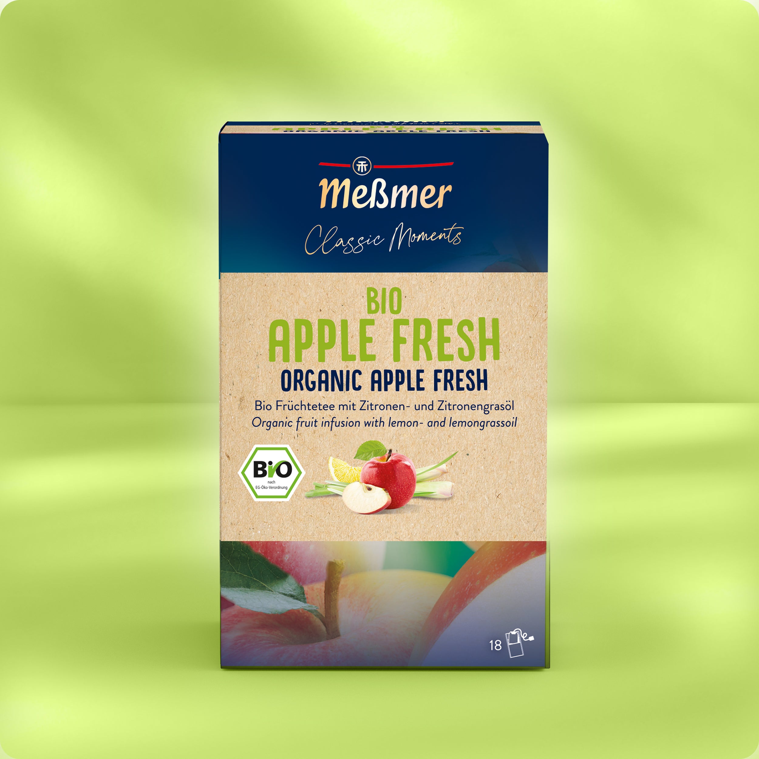 Verpackung von Bio Apple Fresh mit Bio-Siegel, Darstellung von Äpfeln und Zitronengras, Hinweis auf 18 Teebeutel und natürliche Zutaten vor hellgrünem, verschwommenem Hintergrund.