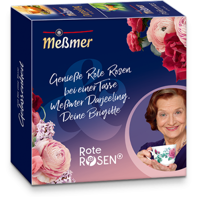 Eine Schachtel Meßmer DE Rote Rosen Tee mit floralen Motiven, deutschem Text und einer lächelnden älteren Frau, die eine Teetasse hält. Die Verpackung hebt die Sorten Darjeeling und Rote Rosen hervor und trägt die Unterschrift von Brigitte.