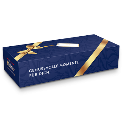 Die Meßmer DE Geschenkbox Klassik ist eine rechteckige blaue Box mit goldenem Band, einem kleinen Blanko-Geschenkanhänger und dem Meßmer-Logo. Darauf steht "GENUSS VOLLE MOMENTE FÜR DICH" - ideal für alle, die gerne Meßmer-Tee auswählen oder genießen.