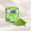 Dose mit Bio Matcha Pulver auf hellem Hintergrund, feines grünes Pulver in aufgeschütteter Form daneben, zeigt die lebendige Farbe und feine Textur des Bio Matcha für die Zubereitung von grünem Tee.
